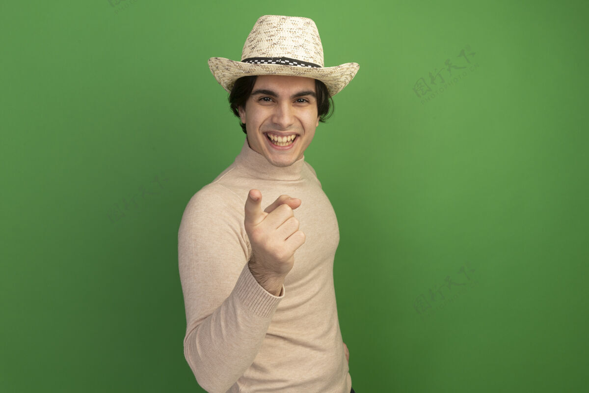 微笑带着微笑的年轻帅哥戴着帽子 在绿色的墙壁上展示你的手势 还有复制空间男人帅气穿