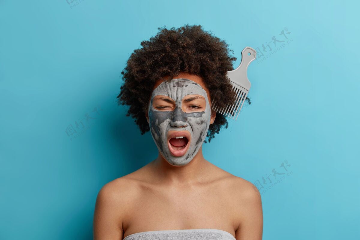 美国身体护理美容概念美丽的黑皮女人用面膜梳在卷发中打呵欠治疗身体蓝色