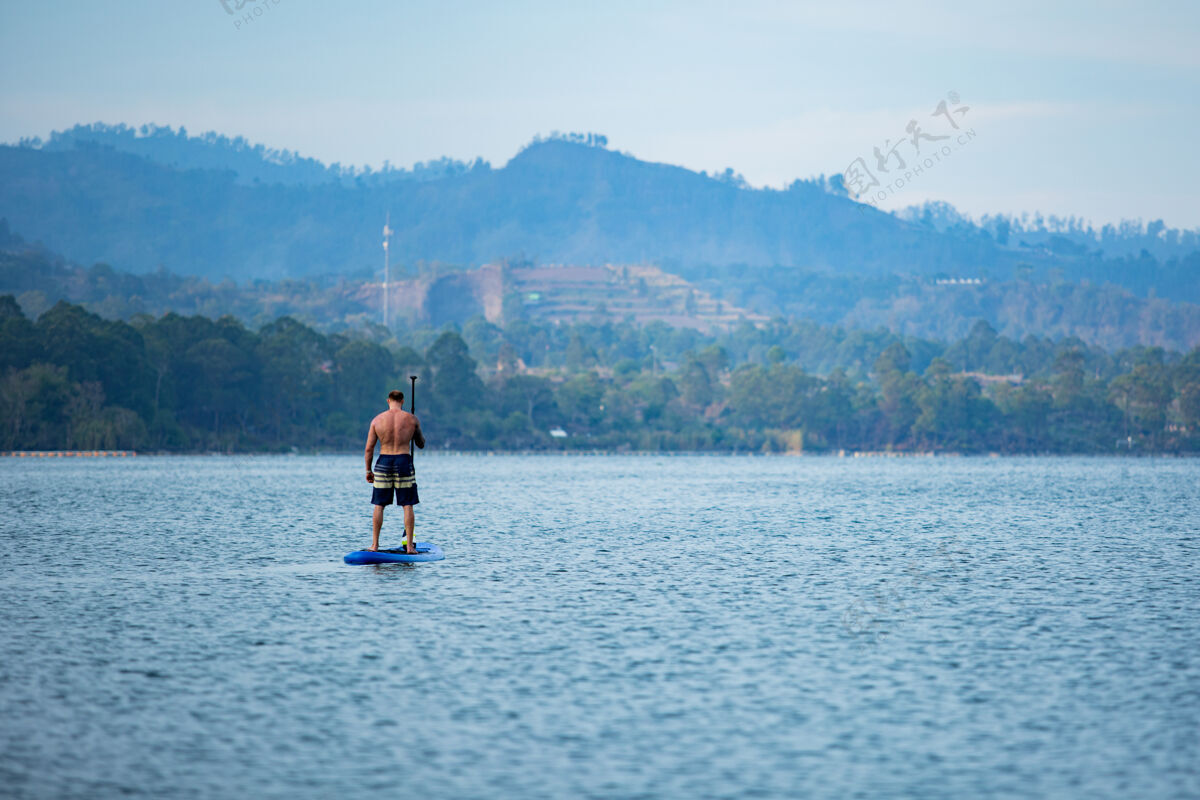 海滩一个男人在湖边骑冲浪板划桨热带娱乐