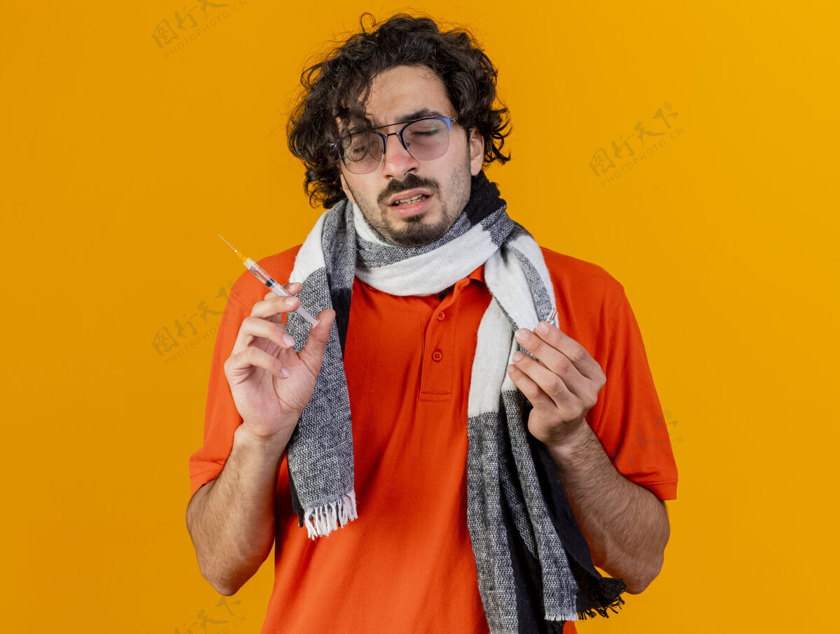 衣服戴着眼镜 戴着围巾 拿着注射器和安瓿 闭着眼睛隔离在橙色墙上的年轻人注射器姿势眼镜