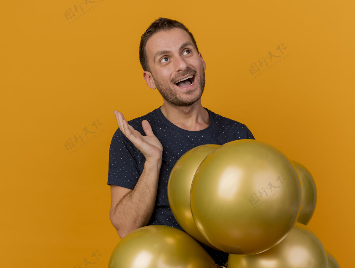 侧身快乐的帅哥拿着氦气球 举手站着 看着橙色墙壁上孤立的一面 还有复制空间衣服表情气球