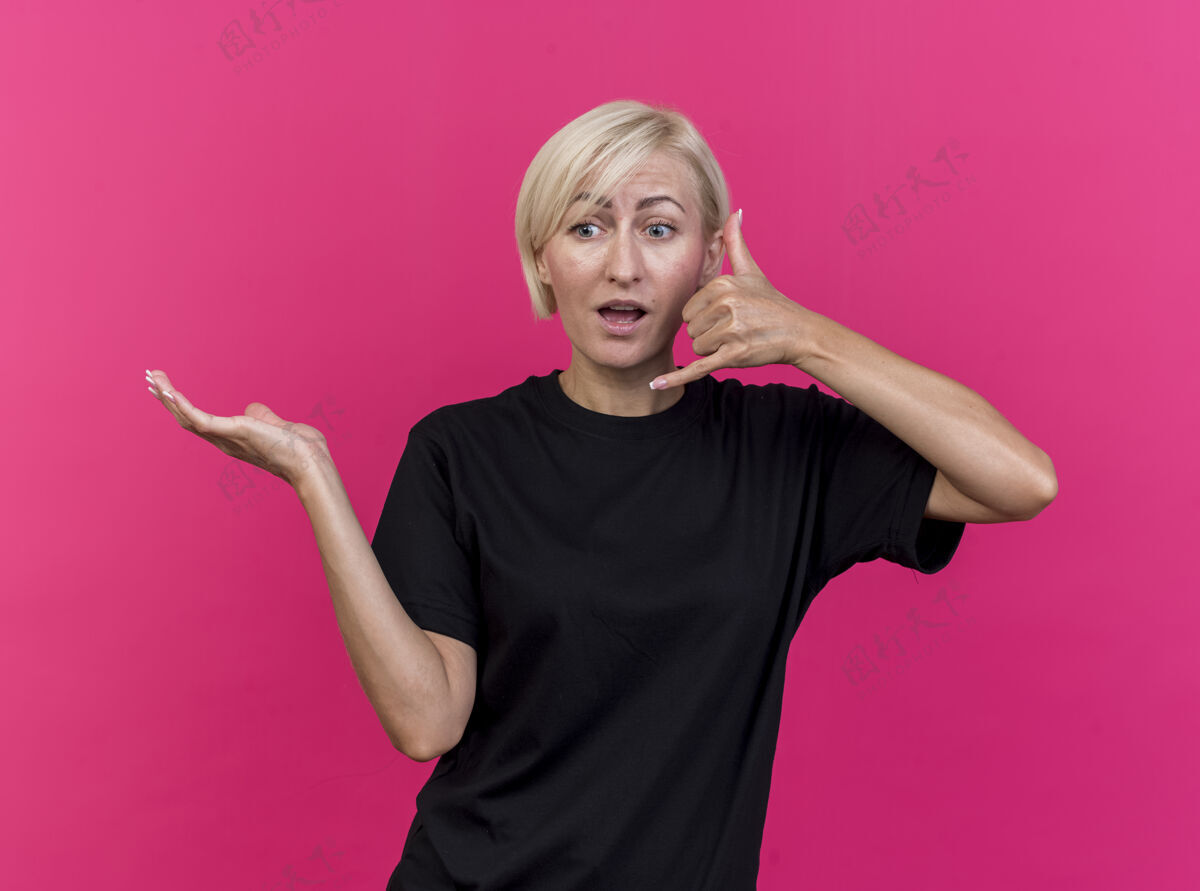 斯拉夫令人印象深刻的中年金发斯拉夫妇女显示空手看在一边做呼叫手势隔离在粉红色的墙上金发手势公民