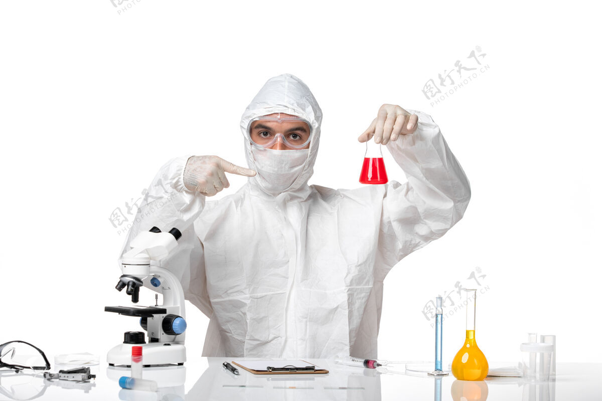 烧瓶正面图：男医生穿着防护服 戴着面罩 因为covid将装有红色溶液的瓶子放在一个空白处到期化学溶液