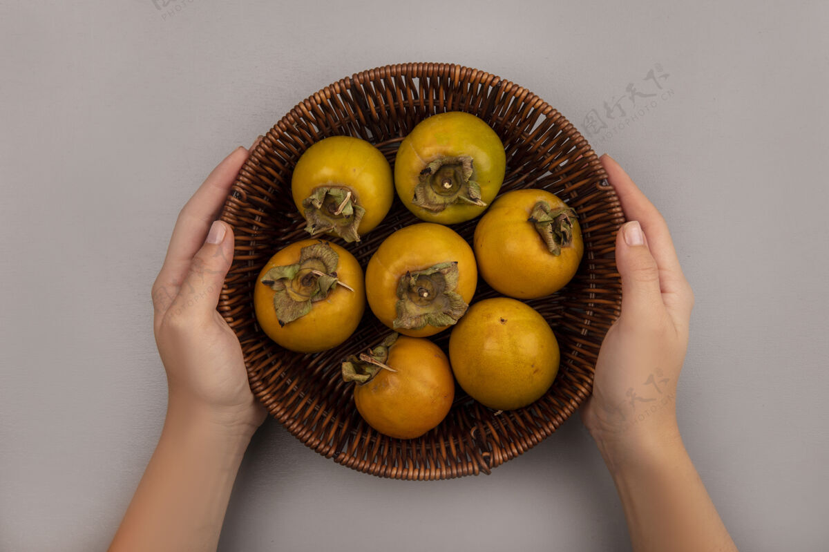视图女性双手捧着一桶柿子水果的俯视图柿子顶部橘子
