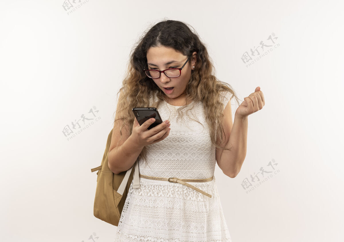 手机印象深刻的年轻漂亮的女学生戴着眼镜 背着书包拿着手机 紧握着拳头 孤零零地看着白色握紧印象手机