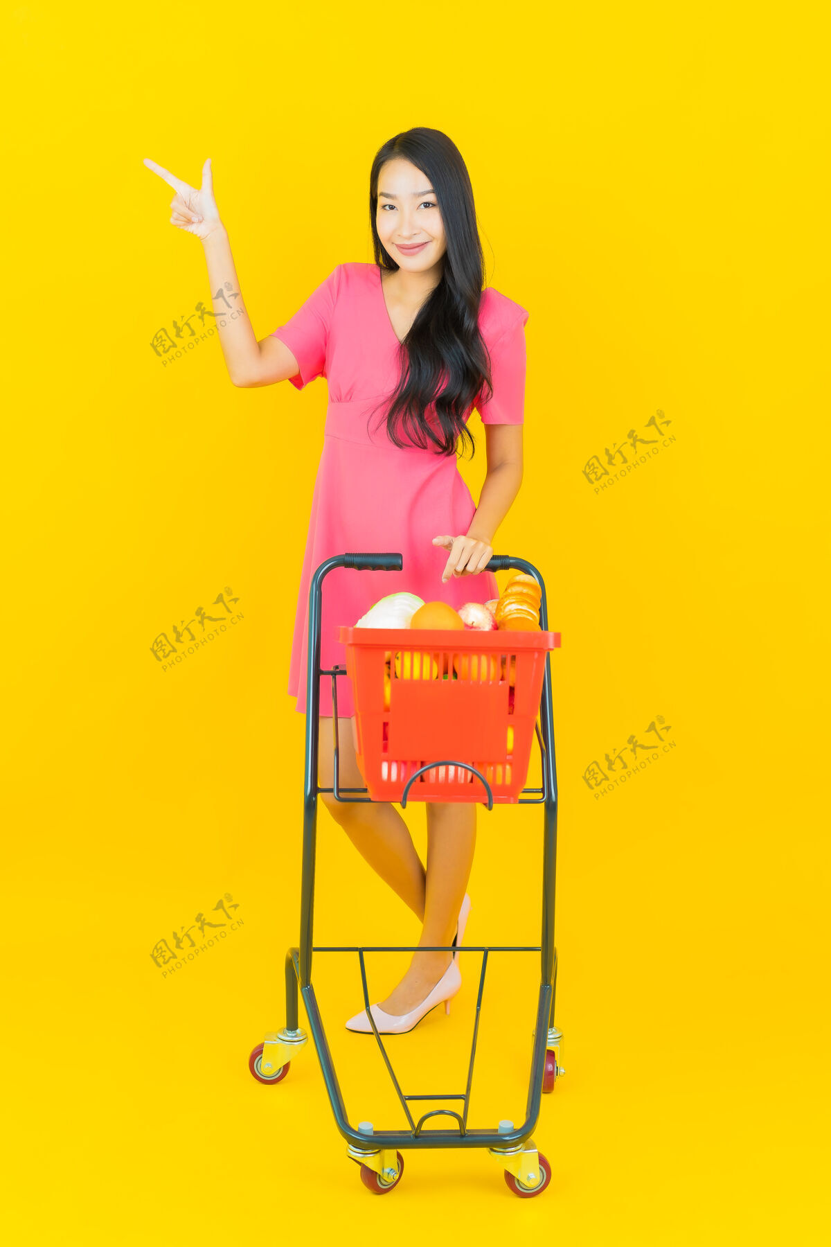 商业一位美丽的亚洲年轻女子微笑着 黄色的墙上挂着超市的购物篮蔬菜销售享受