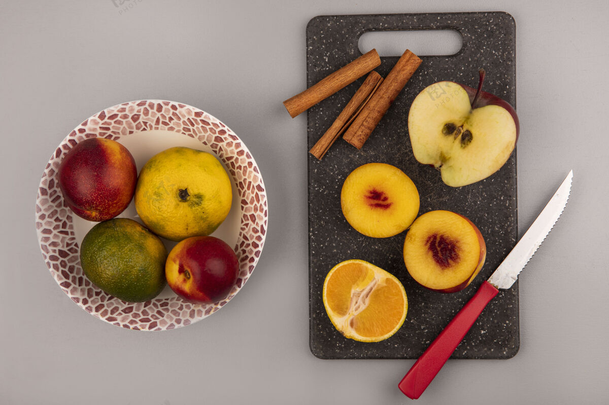 板新鲜的半个桃子放在一个黑色的厨房板上 上面有橘子和苹果 刀子放在一个灰色背景的碗上 上面有桃子和橘子食物一半顶部