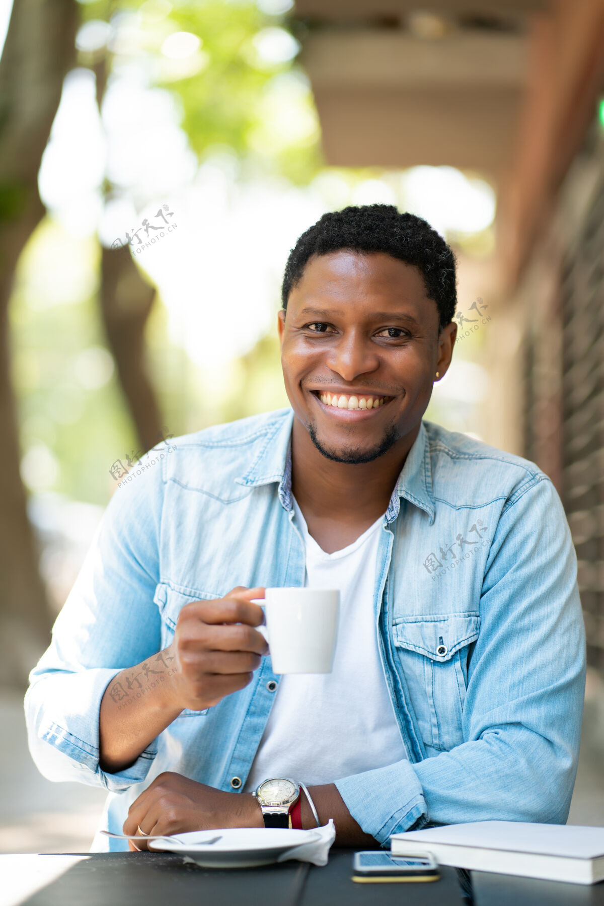 年轻非裔美国人坐在户外的咖啡馆里享受和喝咖啡男性桌子人