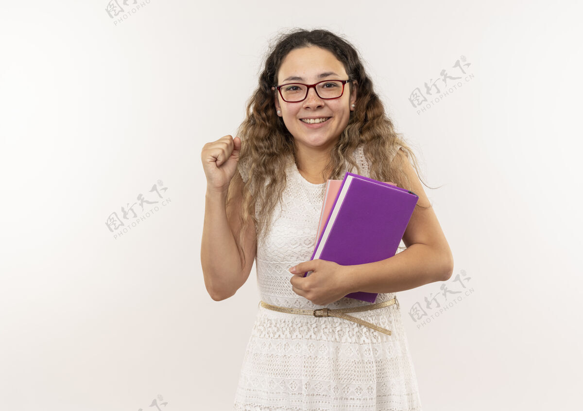 眼镜快乐的年轻漂亮的女学生戴着眼镜拿着书举起拳头孤立在白色拳头抱着戴上