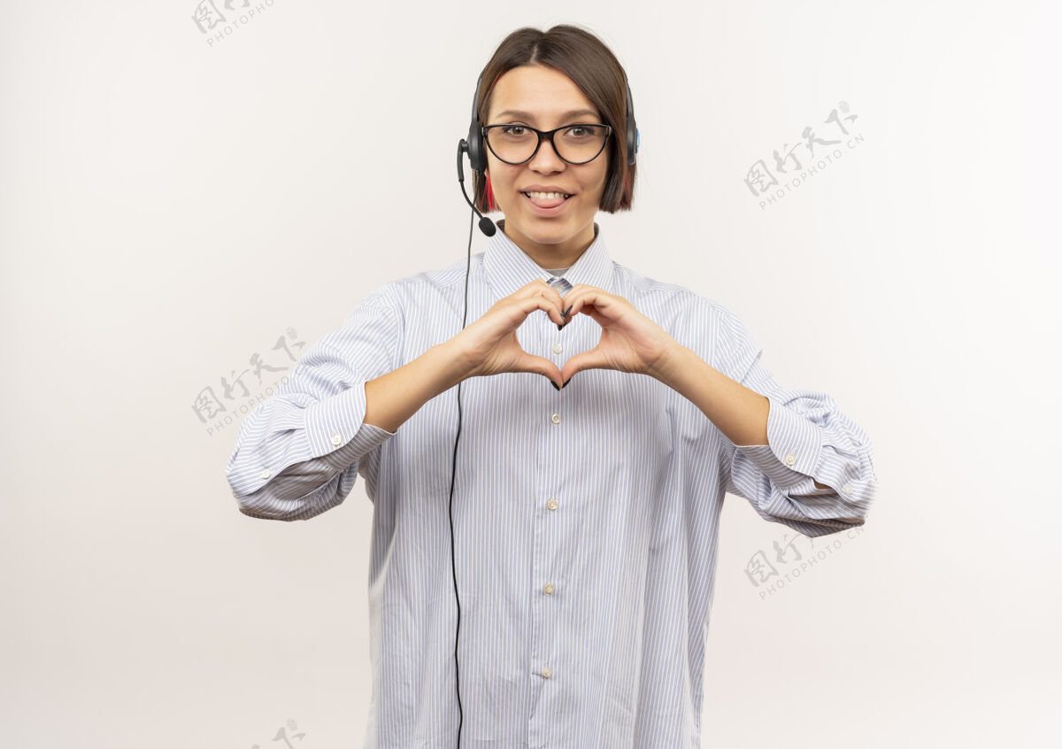 呼叫快乐的年轻呼叫中心女孩戴着眼镜和耳机做心脏标志显示舌头孤立在白色中心展示舌头