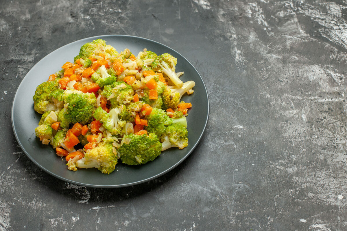 平底锅黑色盘子和灰色桌子上的健康西兰花和胡萝卜餐的侧视图花椰菜餐厅沙拉