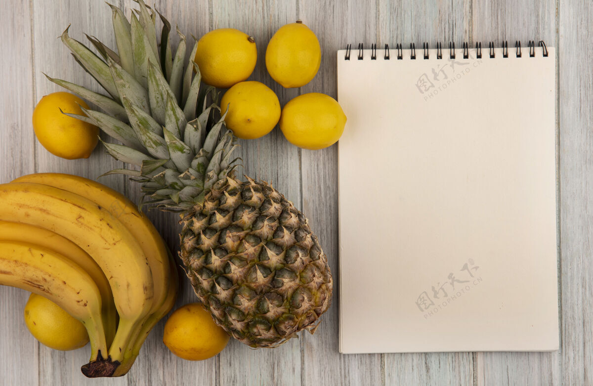 笔记本顶视图富含维生素的水果 如香蕉 菠萝和柠檬隔离在一个灰色的木制背景与复制空间柠檬香蕉食谱