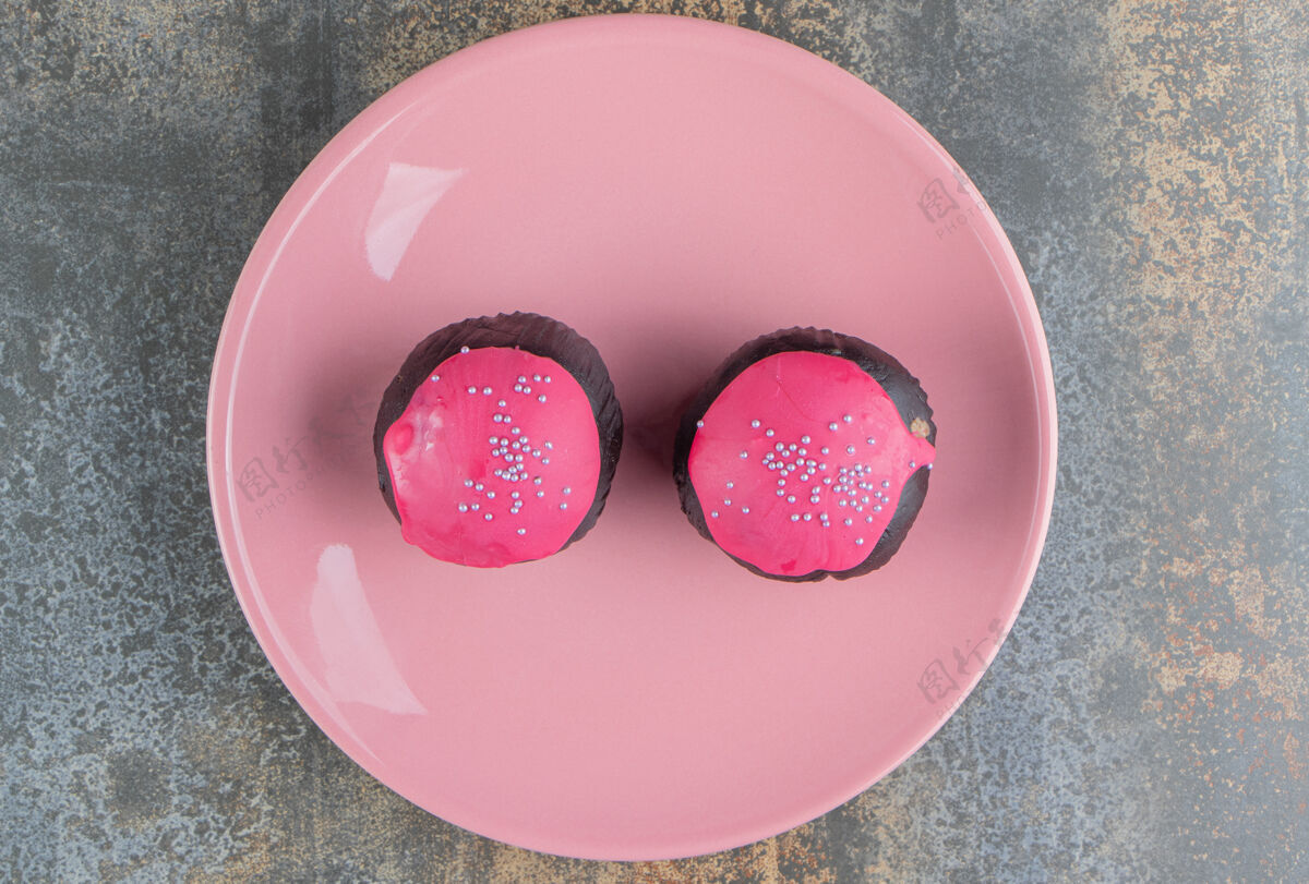 糕点两个甜甜的巧克力甜甜圈 上面撒着粉色的糖霜和花洒烘焙洒蛋糕