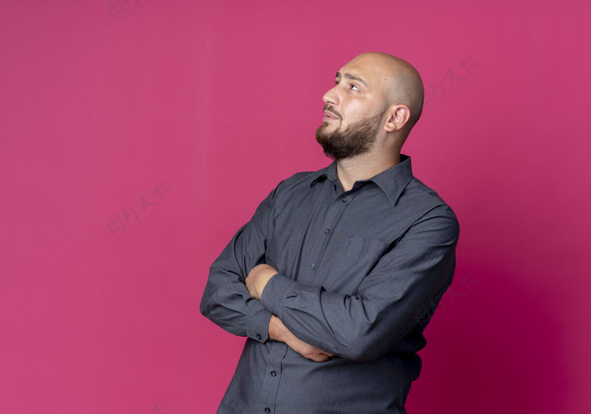 年轻年轻的秃头呼叫中心男子站在封闭的姿态 仰望着孤立的深红色背景与复制空间封闭站立中心