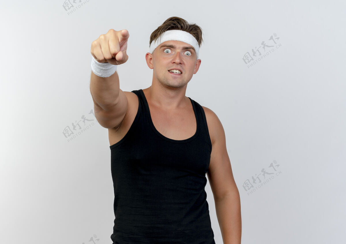 腕带印象深刻的年轻英俊的运动男子戴着头带和腕带指着前面孤立的白色穿运动男人