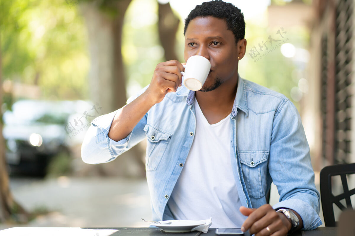 时间非裔美国人坐在户外的咖啡馆里享受和喝咖啡杯子欢呼桌子