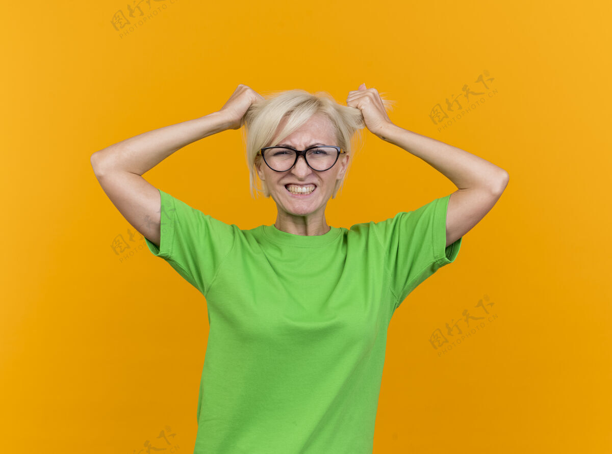 脸紧张的中年金发斯拉夫女人戴着眼镜看着前面拉着头发隔离在黄色的墙上斯拉夫姿势立场