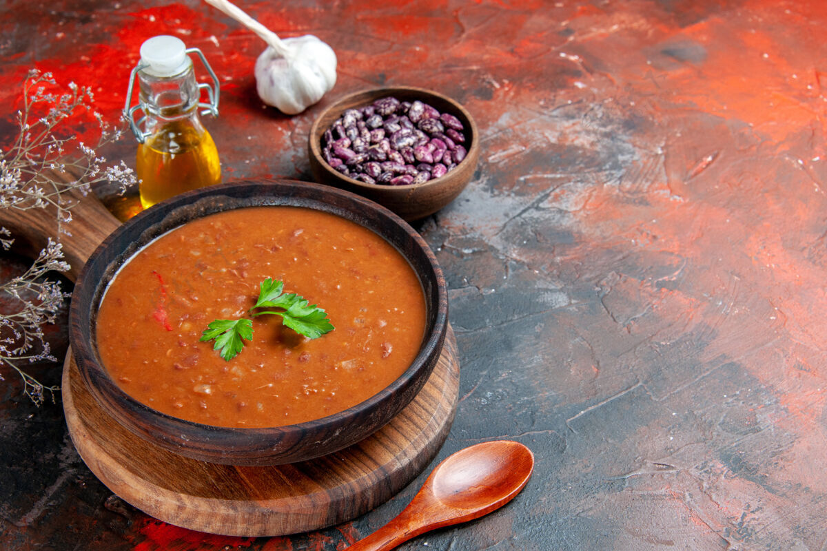 横切棕色砧板上的番茄汤和混色桌上的油瓶的水平视图碗汤碗餐