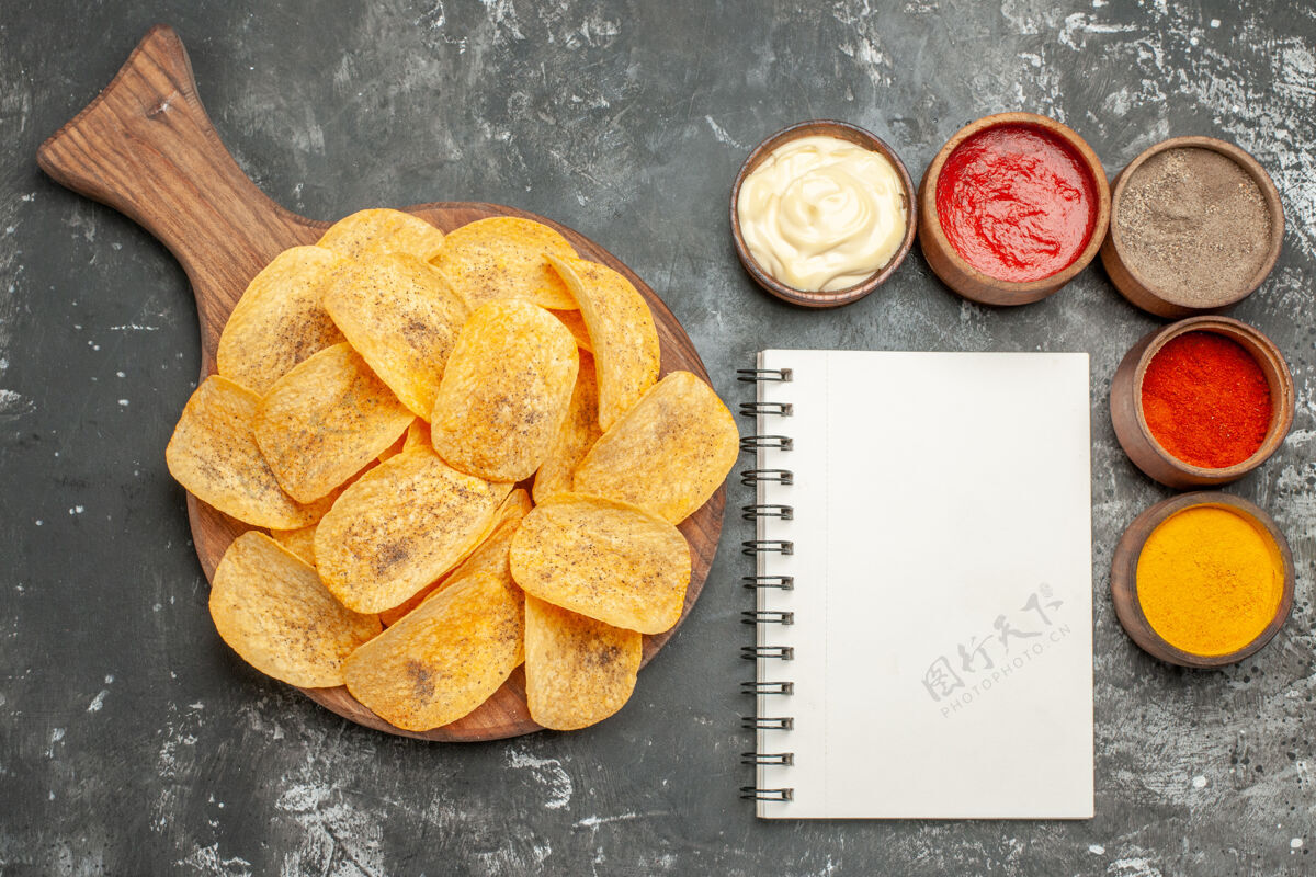 番茄酱在灰色的桌子上可以看到土豆片 香料和蛋黄酱 番茄酱和笔记本的水平视图零食薯片面包