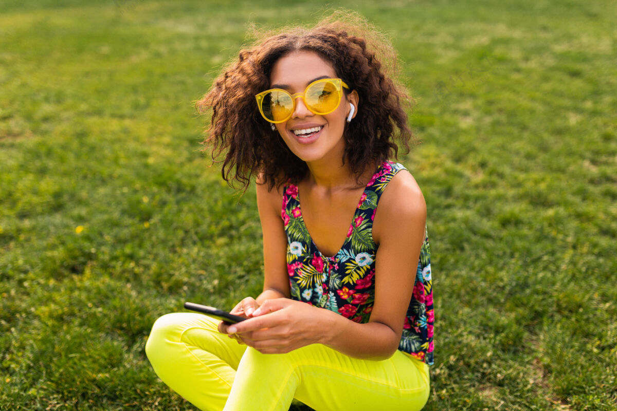 音乐年轻时尚微笑的黑人女子使用智能手机 通过无线耳机听音乐 在公园里玩得很开心眼镜女孩兴奋