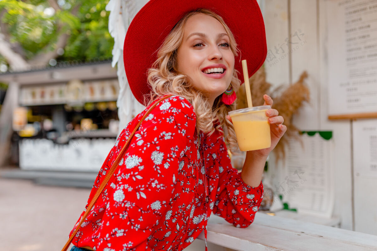 外面迷人时尚的金发微笑女士 头戴草帽 身穿短衫 夏季时尚套装 饮用天然水果鸡尾酒冰沙果汁明亮持有