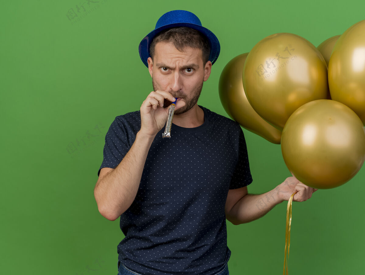 哨子戴着蓝色派对帽的白种人帅哥拿着氦气球吹着哨子 在绿色背景上隔离开来 留有复制空间人不愉快气球