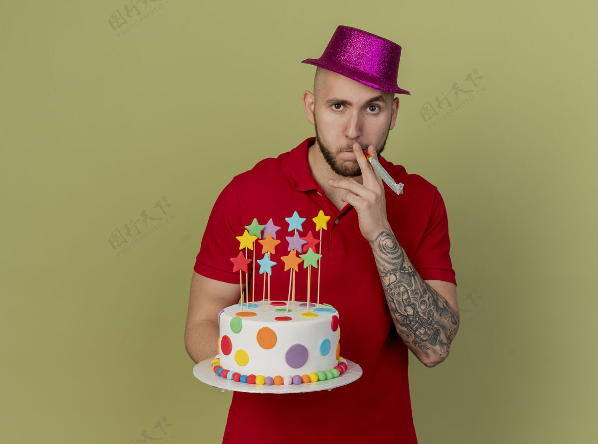 斯拉夫人自信的年轻英俊的斯拉夫派对男孩戴着派对帽拿着生日蛋糕看着相机拿着派对吹风机在橄榄绿的背景上孤立的复制空间帽子复制嘴巴
