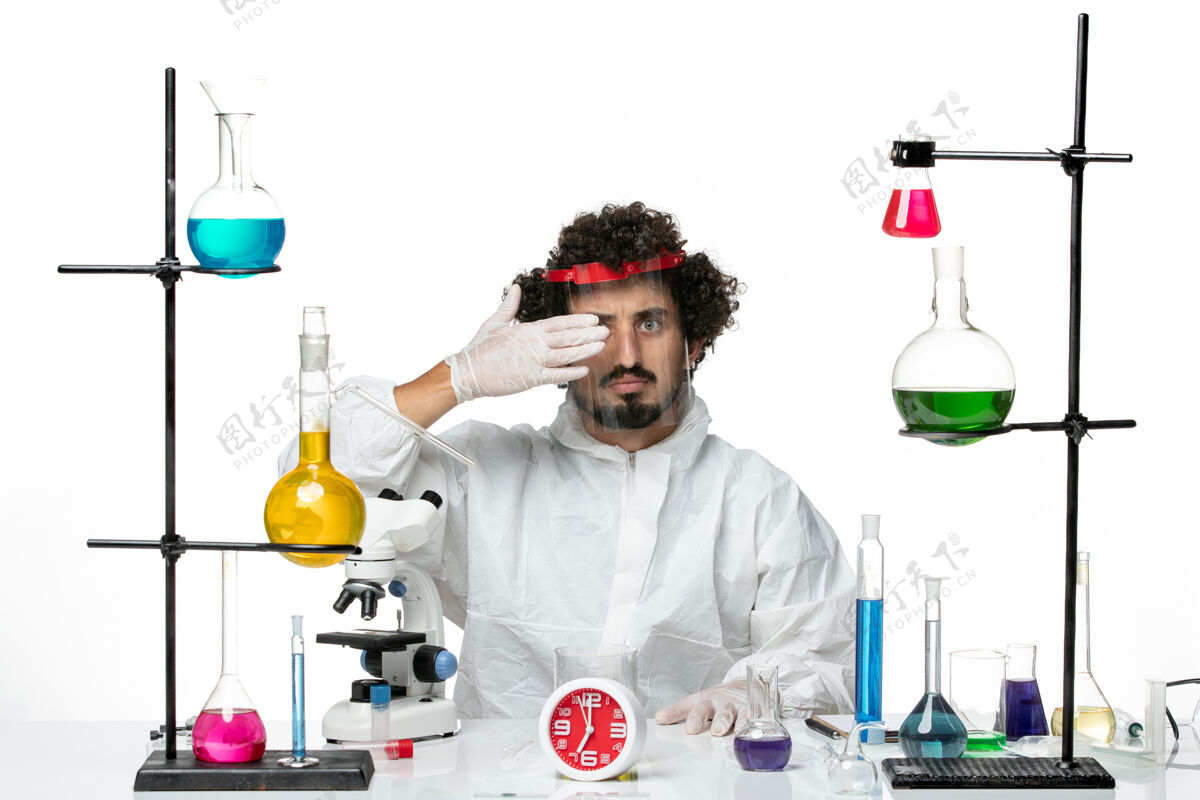 穿着正面图年轻的男科学家穿着特殊的西装 戴着防护头盔 在白色的办公桌上工作 科学实验室里充满了男性化学特殊实验室套装
