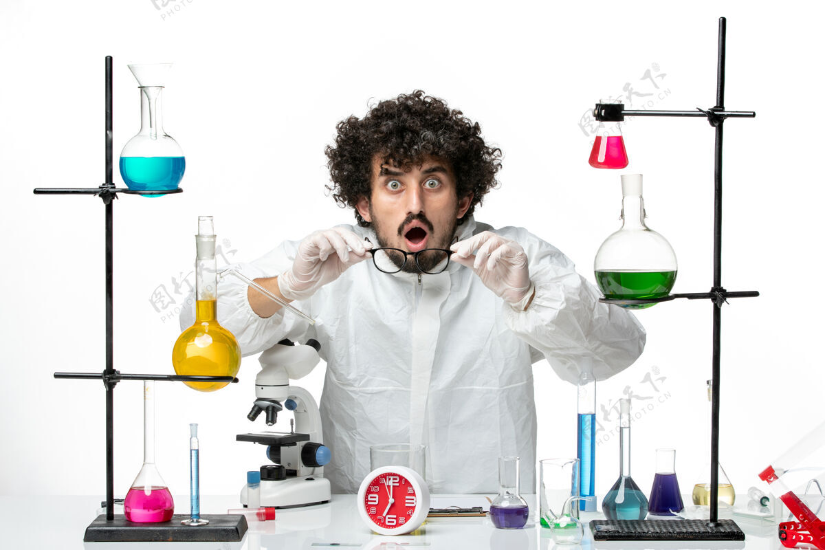 溶液正面图：身着特殊套装的年轻男性科学家站在白墙实验室的桌子旁 拿着解决方案支架科学化学