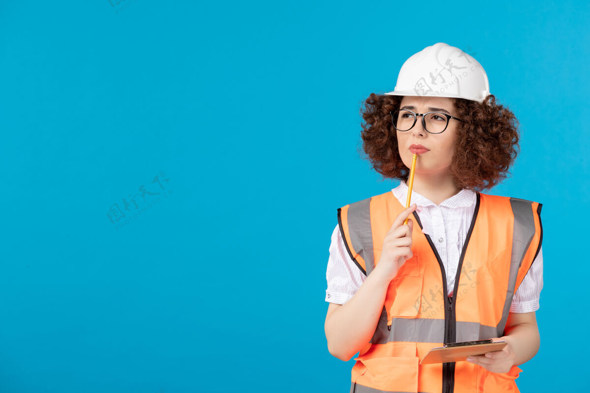 背心前视图：蓝色墙上穿着制服戴着头盔的女建筑工人蓝色建筑工人制服