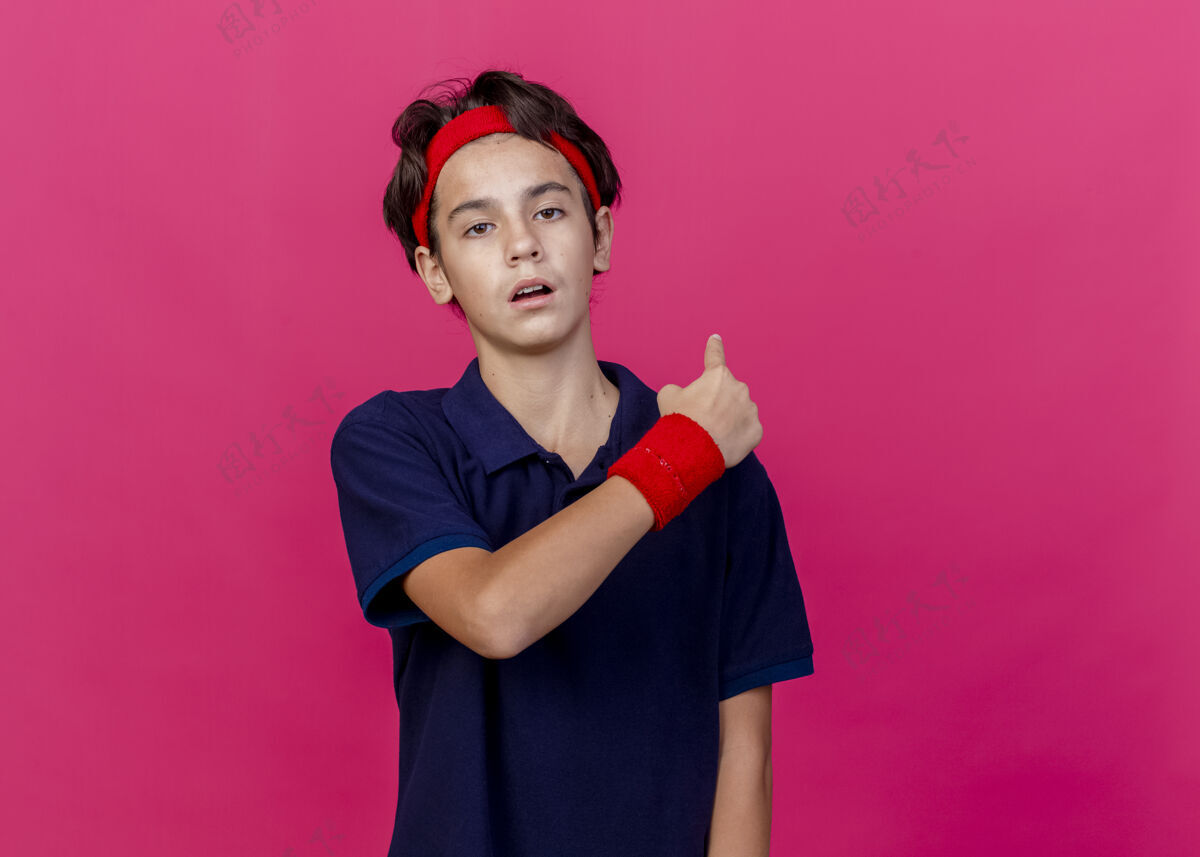男孩年轻帅气的运动男孩戴着头带和戴着牙套的腕带 看着摄像机指向身后 在深红的背景上 有着一个复制空间腕带空间深红色