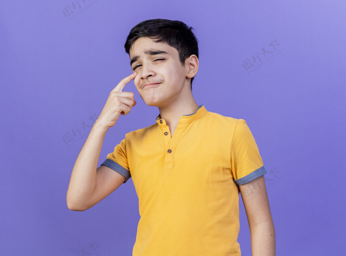 男孩悲伤的年轻白人男孩看着相机把手指放在眼睛下面孤立的紫色背景上年轻手指悲伤