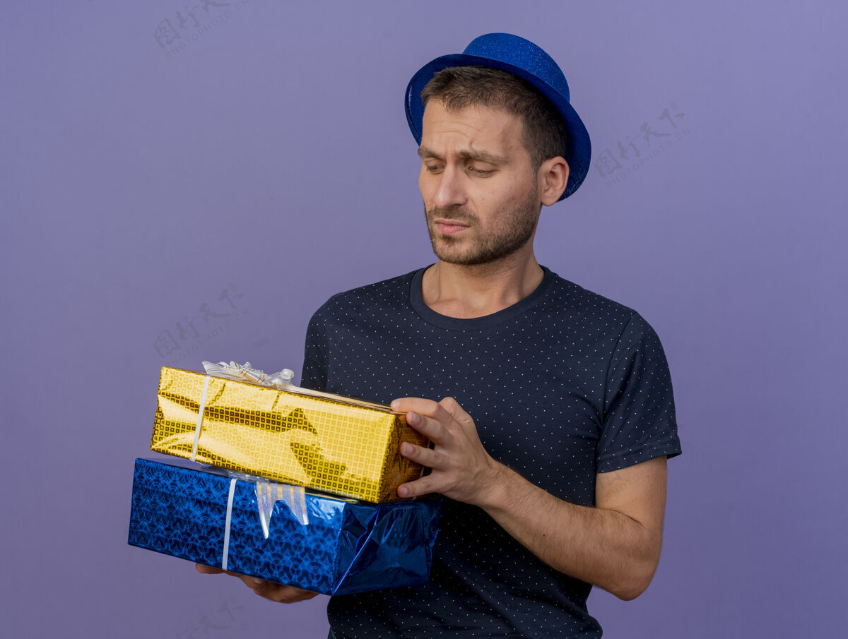礼物戴着蓝色帽子的白种人帅哥拿着礼物盒 看着紫色背景上的礼物盒 上面留着复印空间盒子空间紫色
