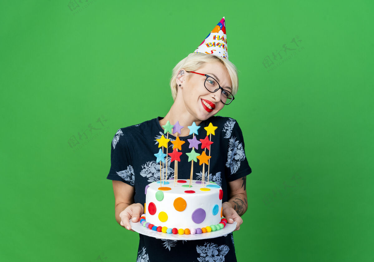 派对微笑的年轻金发派对女孩戴着眼镜 戴着生日帽 拿着生日蛋糕 星星们看着隔离在绿色背景上的一面 还有复制空间金发抱着女孩