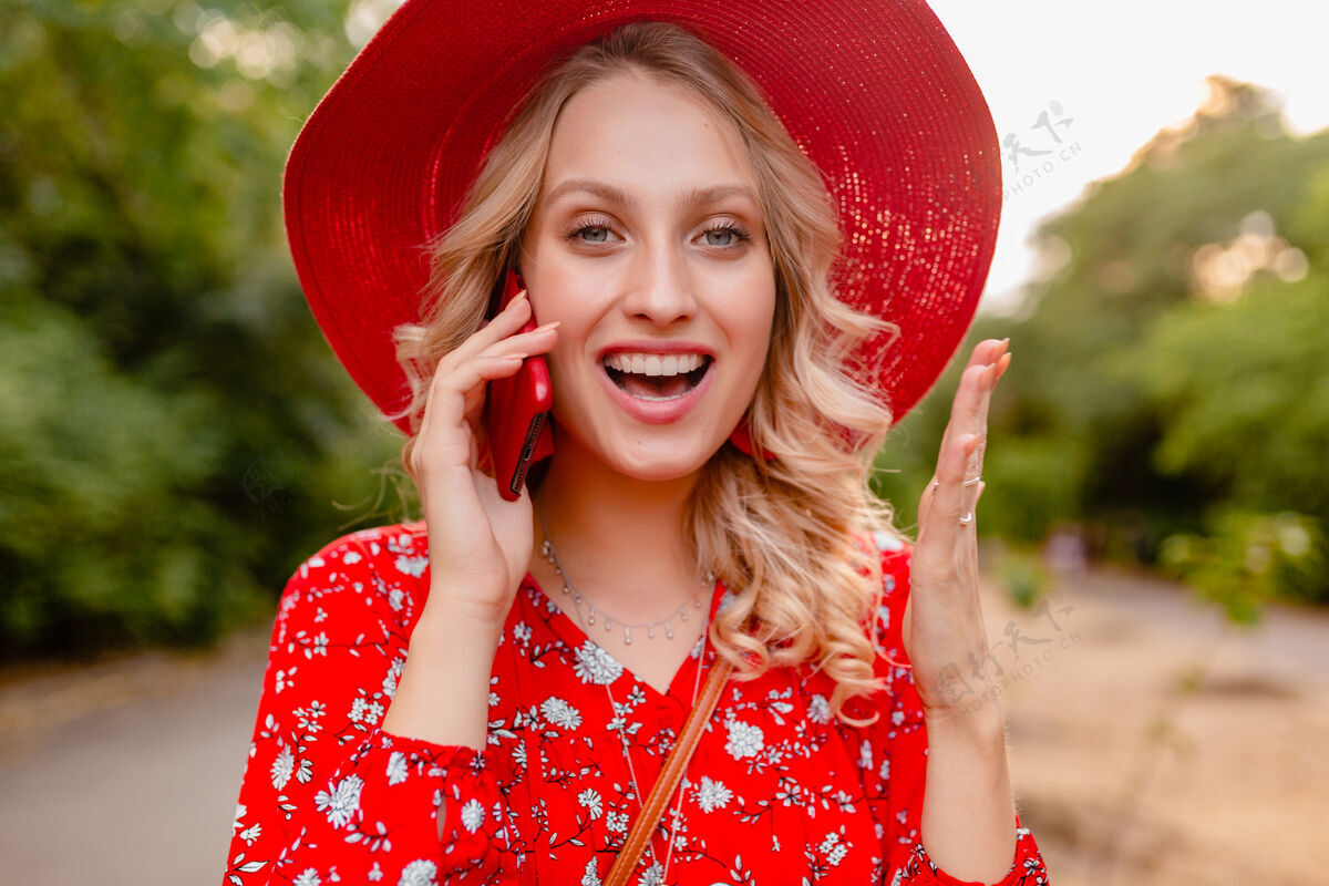 白色迷人的时尚金发微笑的妇女在稻草红色帽子和衬衫夏季时尚服装画像在电话交谈积极的姿态情感年轻情感享受