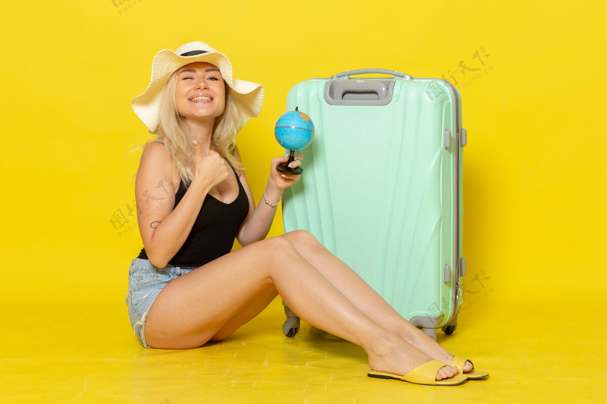 海正面图度假中的年轻女性坐在她的绿色袋子里拿着地球仪在黄色的墙上女性旅行旅行海色太阳颜色地球年轻