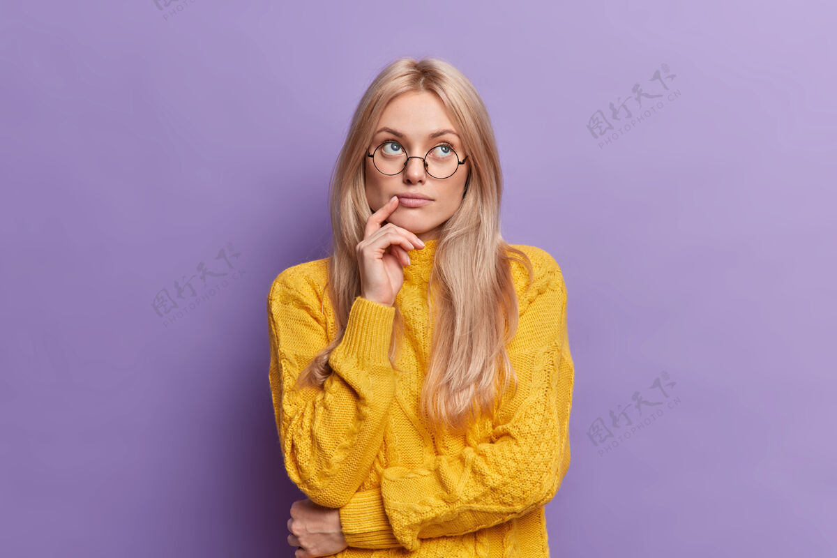 针织年轻漂亮的年轻女子思想集中在站着体贴 手放在脸上站着体贴的姿势戴着圆眼镜黄毛衣自然思考休闲