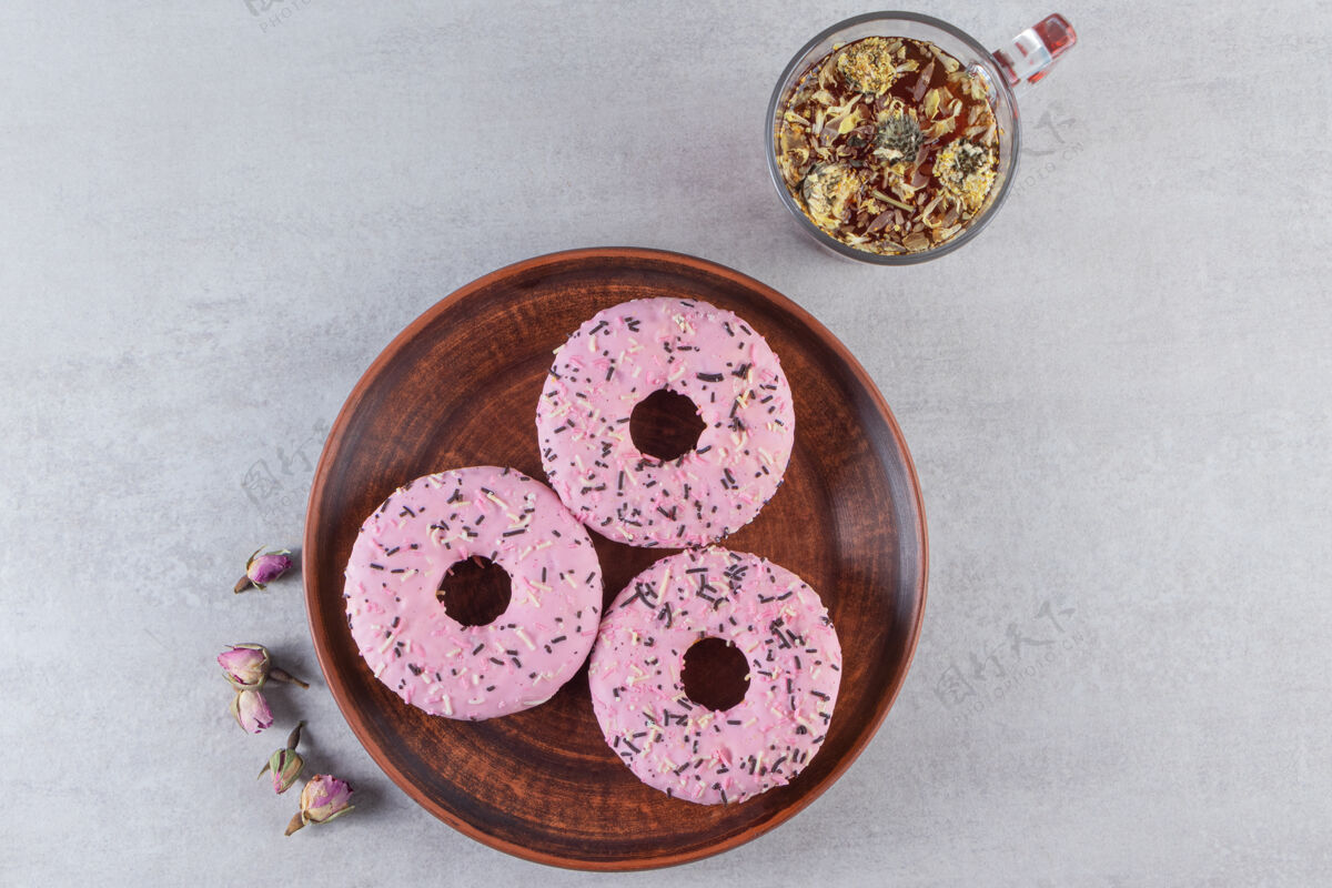 釉一盘粉红色甜甜圈和一杯热茶放在石头表面甜点饼干糕点