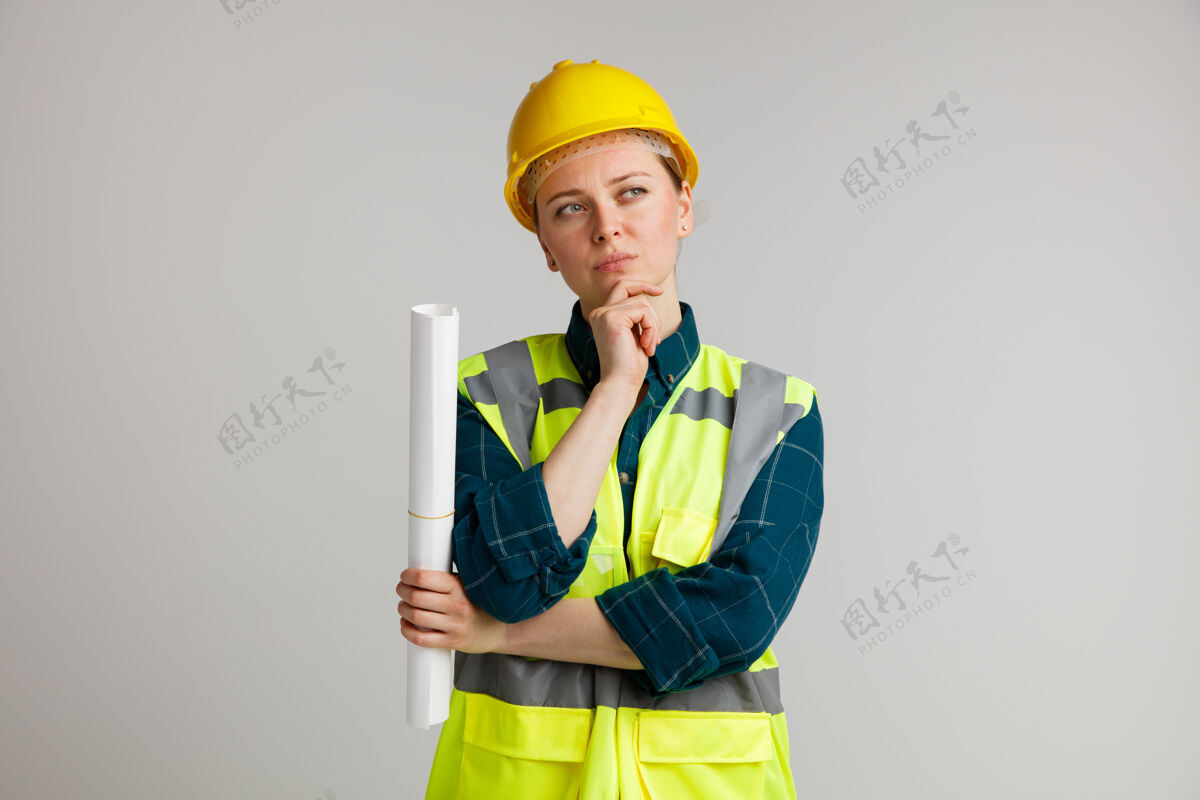 年轻体贴的年轻女建筑工人戴着安全帽 穿着安全背心 手里拿着纸 手放在下巴上 看着旁边头盔工人下巴