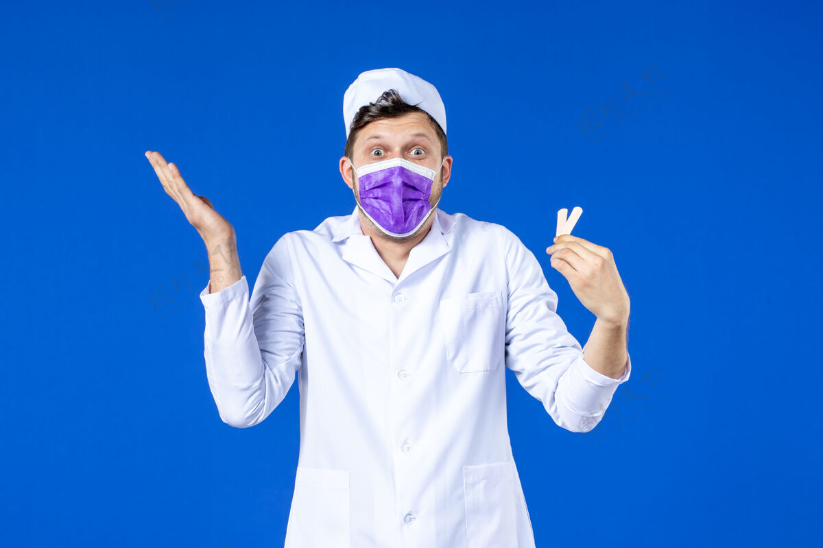 医院前视图中的男医生穿着医疗服和面具举行小医疗补丁蓝色衣服男医生大流行
