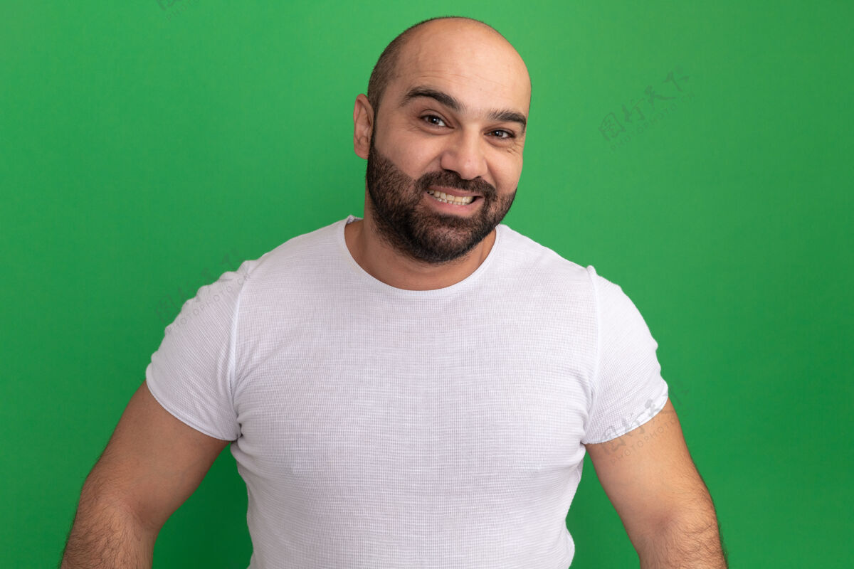 伙计快乐的胡子男人穿着白色t恤 站在绿色的墙壁上愉快地微笑着胡子站起来加油