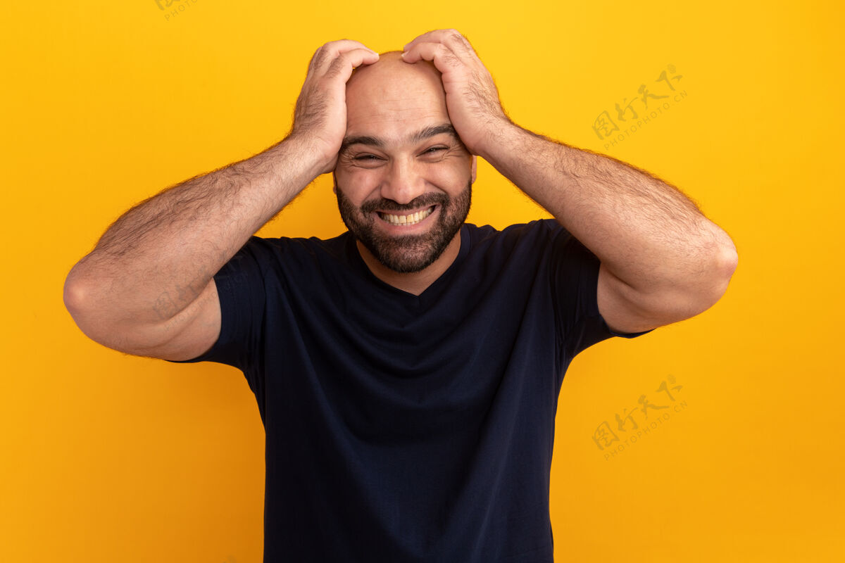 站立一个留着大胡子的男人穿着海军t恤 手放在头上站在橘色的墙上 看上去既困惑又沮丧困惑沮丧头