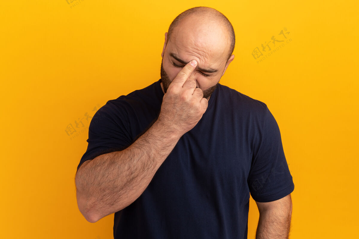 额头一个穿着海军t恤的大胡子男人站在橘色的墙上摸着他的额头 又累又无聊 头痛头痛站着男人