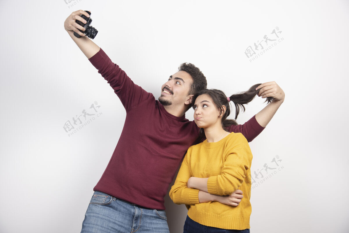 年轻一对可爱的情侣拿着相机自拍 在白墙上摆姿势爱约会男人