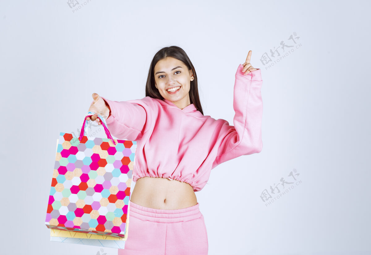 照片女孩拿着五颜六色的购物袋 指着上面的某个地方时尚年轻人雇员