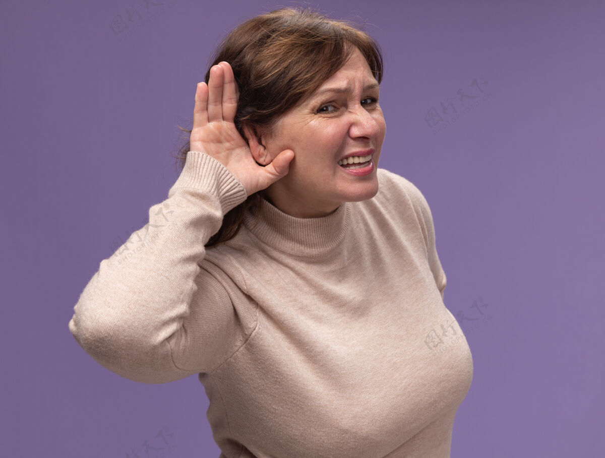 站穿米色套头衫的中年妇女 手捂着耳朵 站在紫色的墙上听闲话八卦高领毛衣女人