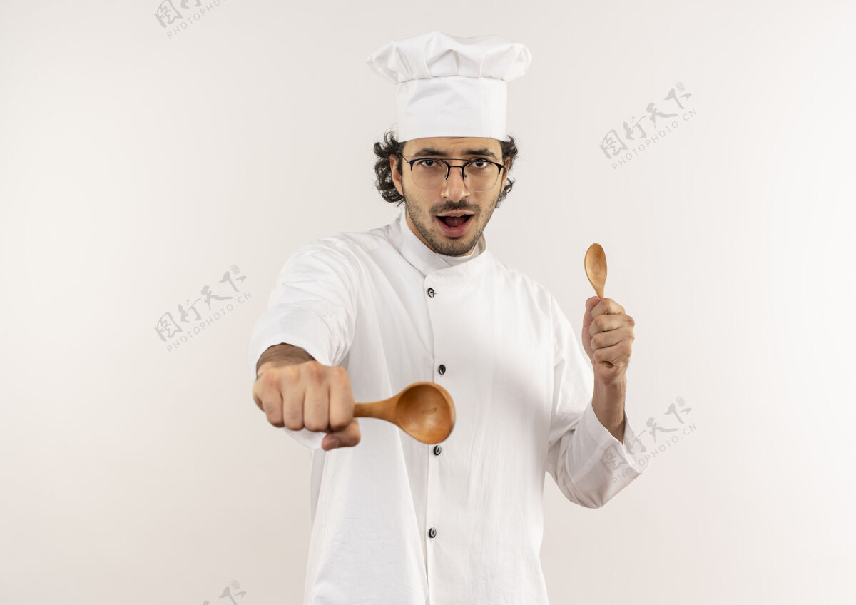 拿着快乐的年轻男厨师穿着厨师制服 戴着眼镜拿着勺子年轻眼镜男