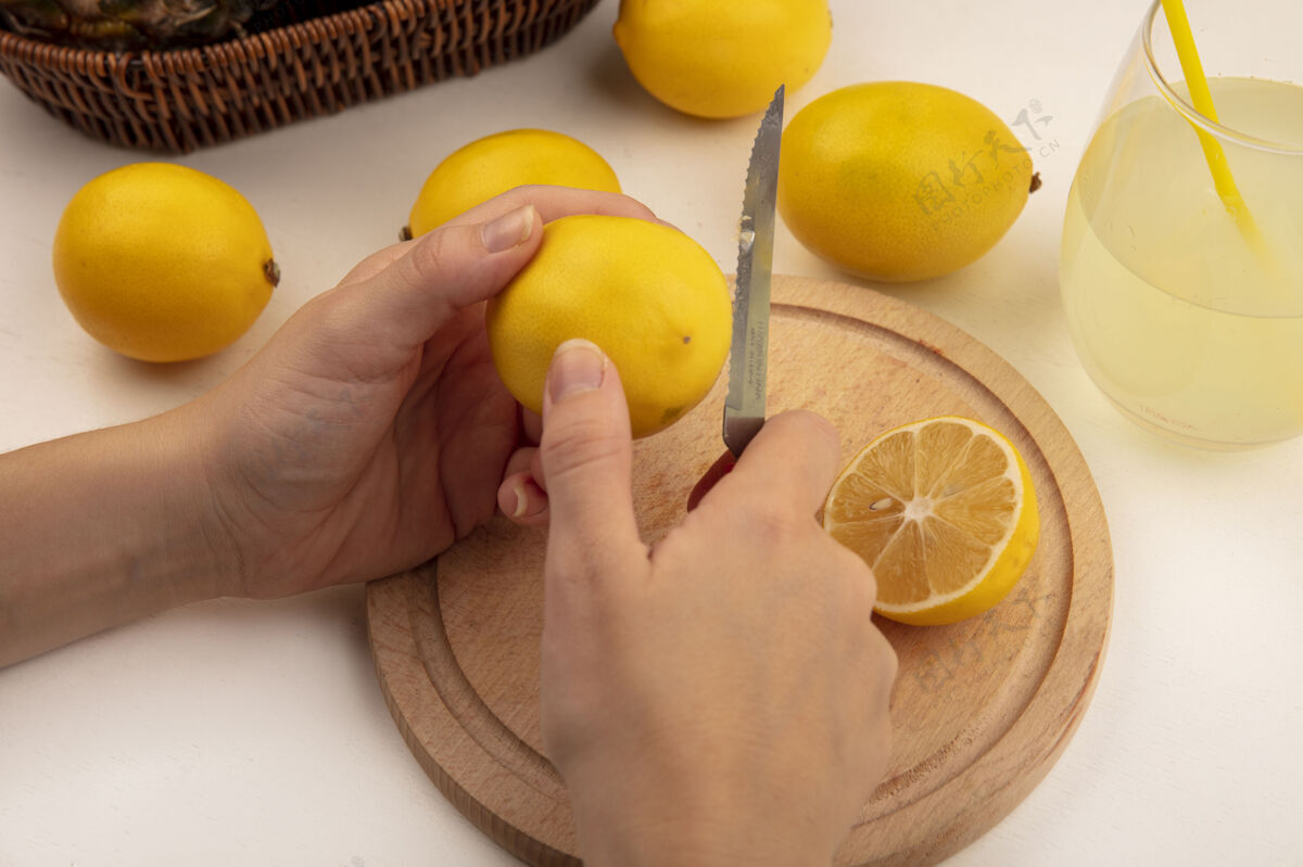 刀俯视图中的女性手切割新鲜的柠檬在一个木制的厨房板与柠檬和柠檬汁刀在一个白色的表面木材新鲜美味