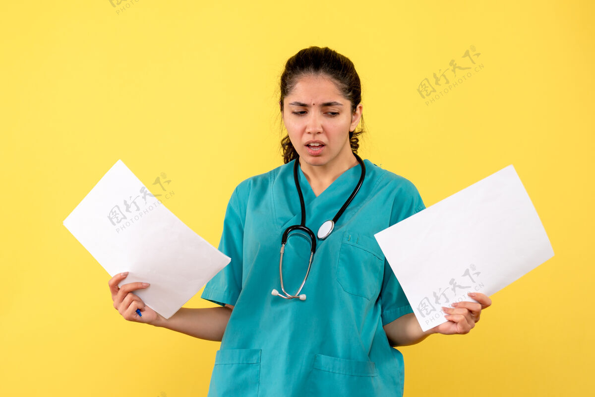 持有前视图困惑的女医生拿着文件站在黄色背景上制服诊所人