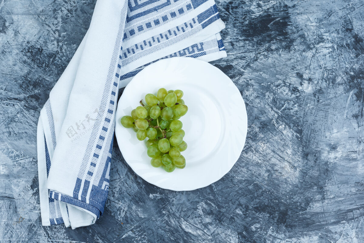 厨房将白葡萄平铺在白色盘子里 厨房毛巾放在深蓝色大理石背景上水平美味水果横